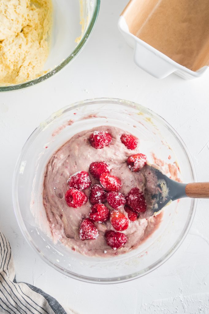 A loaf batter with raspberries getting mixed in with a large spoon.