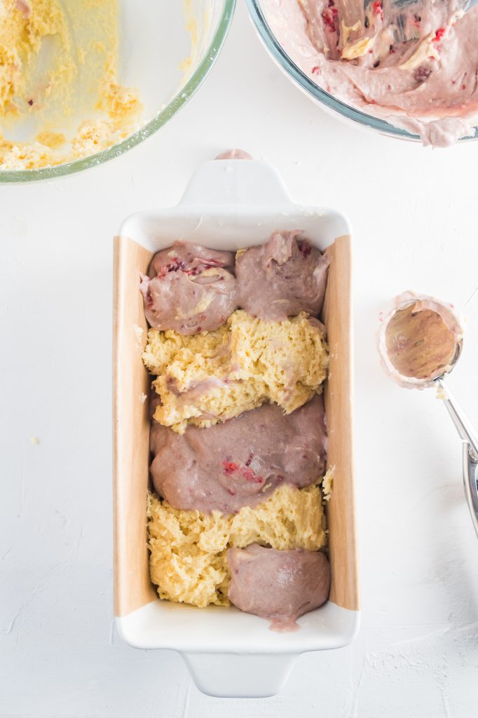 Plain batter and raspberry battery are set in an alternating pattern in a loaf tin.