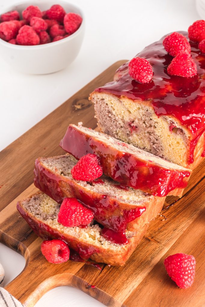 A sliced raspberry marble loaf accented with fresh raspberries sitting on a wooden cutting board.