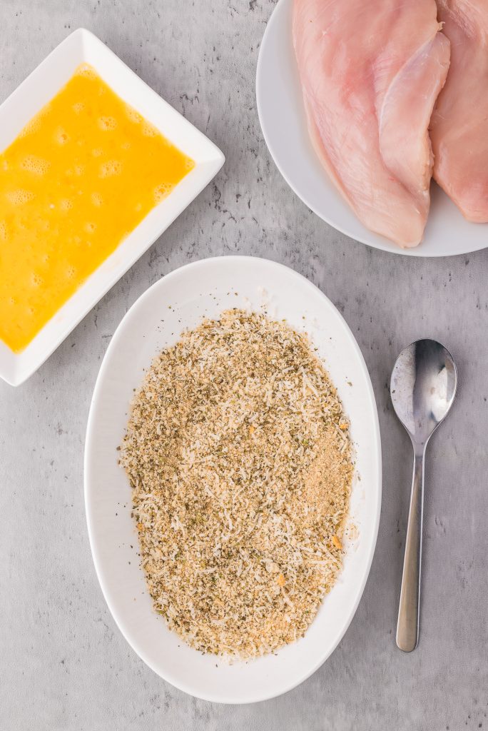 A shallow bowl filled with spiced breadcrumbs. Egg and chicken are in the corners.