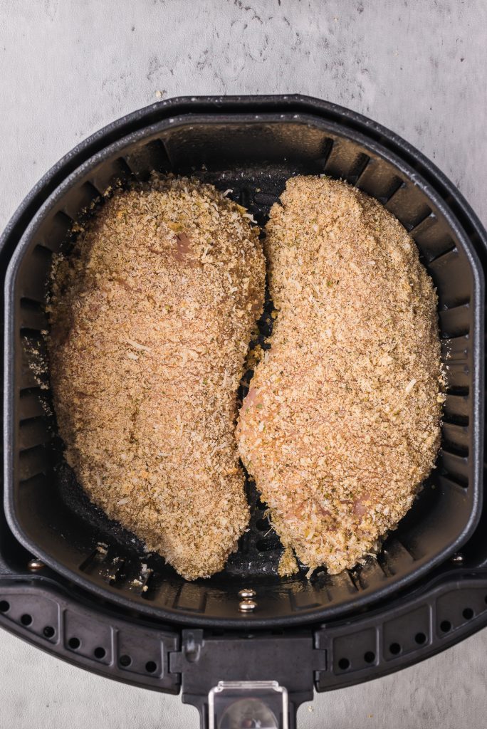 Two pieces of raw, breaded chicken in an air fryer basket.