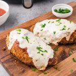 Two pieces of air fryer chicken parmesan on a wooden cutting board.