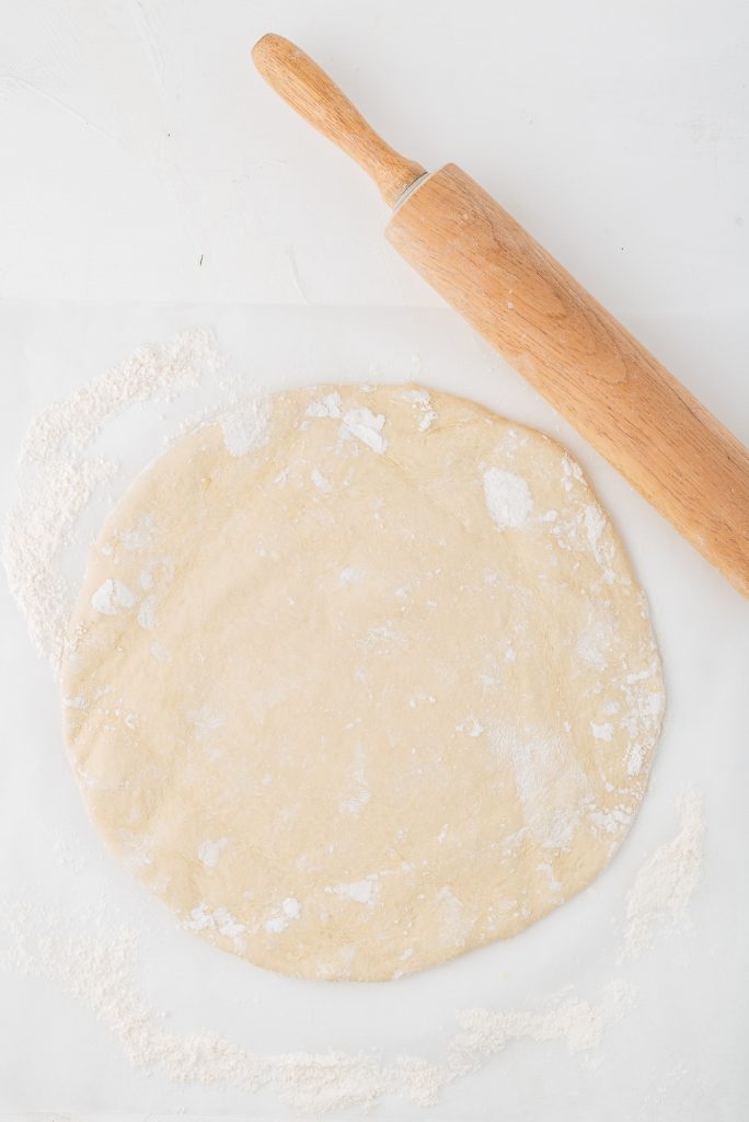 A ball of dough rolled flat into a large circle next to a rolling pin.