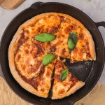 A cast iron pizza in the pan with one slice removed.