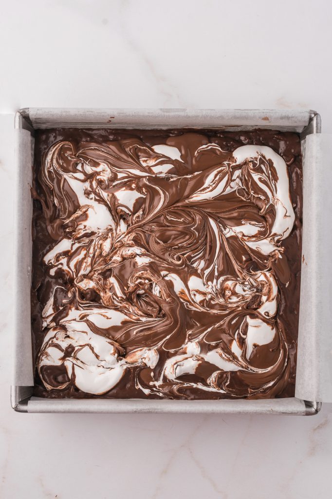 The mixed brownie batter topped with a marbled layer of nutella and marshmallow fluff in a parchment lined brownie tray.