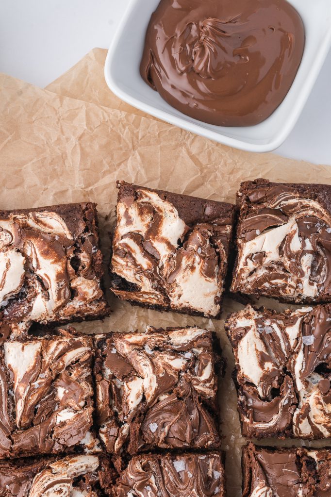 Six sliced nutella fluff brownies on some parchment paper next to a bowl of nutella.