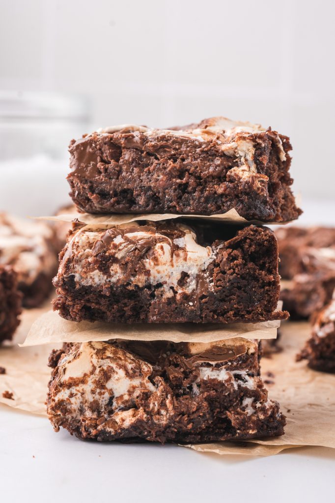 A stack of three gooey nutella fluff brownies separated by squares of parchment paper.