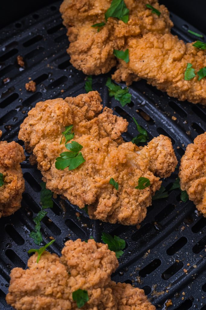 A closeup of the cooked Air Fryer Frozen Chicken Tenders in the air fryer basket sprinkled with green onions.