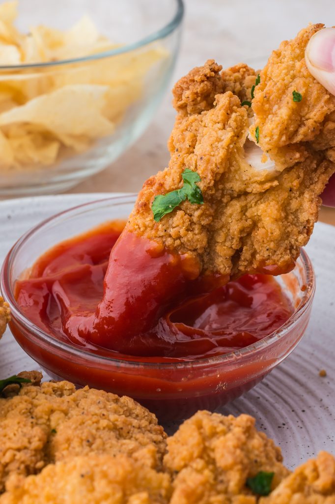 A closeup of a cooked Air Fryer Frozen Chicken tender being dipped into ketchup.