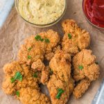 A tray of cooked Air Fryer Frozen Chicken Tenders with mustard and ketchup in two small glass bowls.