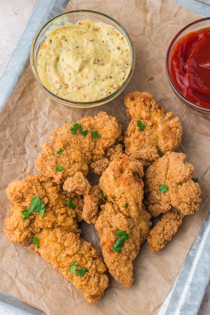 A tray of Air Fryer Frozen Chicken Tenders with mustard and ketchup in two small glass bowls.