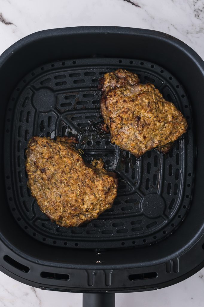 Two cooked steaks topped with the dijon mixture in an air fryer basket.