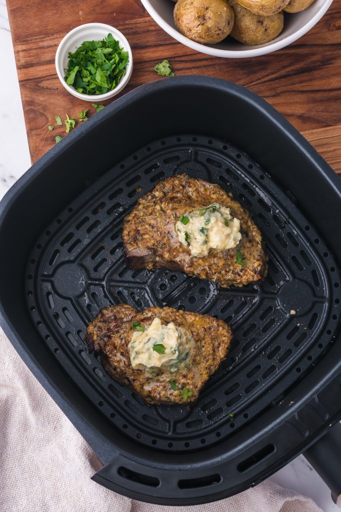 Two Air Fryer Steaks with Garlic Butter inside the air fryer basket.