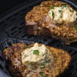 A close up of two Air Fryer Steaks with Garlic Butter inside the air fryer basket.