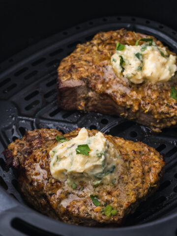 A close up of two Air Fryer Steaks with Garlic Butter inside the air fryer basket.