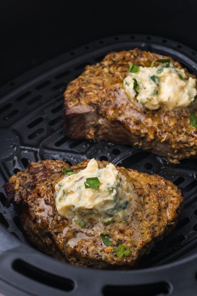 A close up of two Air Fryer Steaks with Garlic Butter inside the air fryer basket.