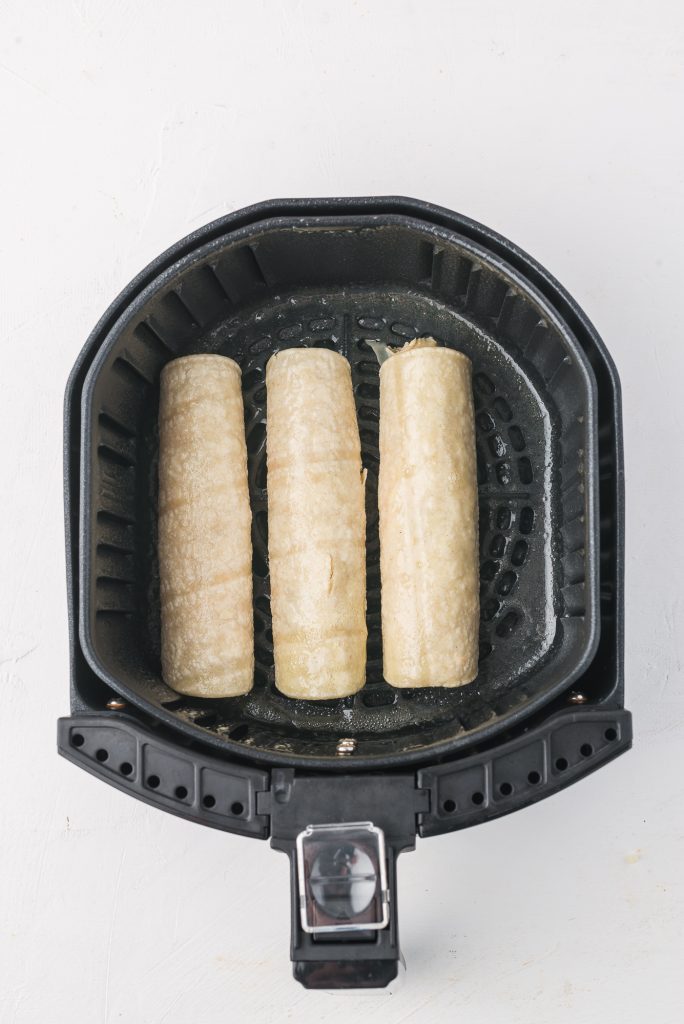 Three Air Fryer Chicken and Cheese Taquitos in the basket of an air fryer.