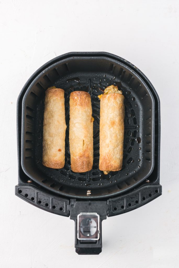 Three fully cooked Air Fryer Chicken and Cheese Taquitos in the basket of an air fryer.