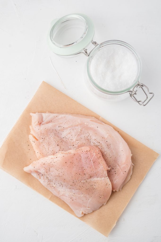 Two raw pieces of chicken breast next to a small salt cellar.