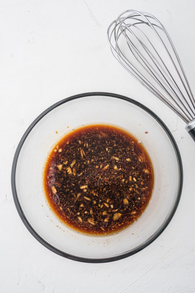 The combined dressing in a glass bowl next to a whisk.