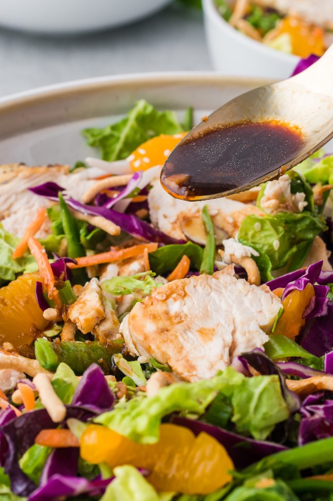 A close-up of a spoonful of dressing being poured over the completed Chinese Style Chicken Salad with Cabbage.