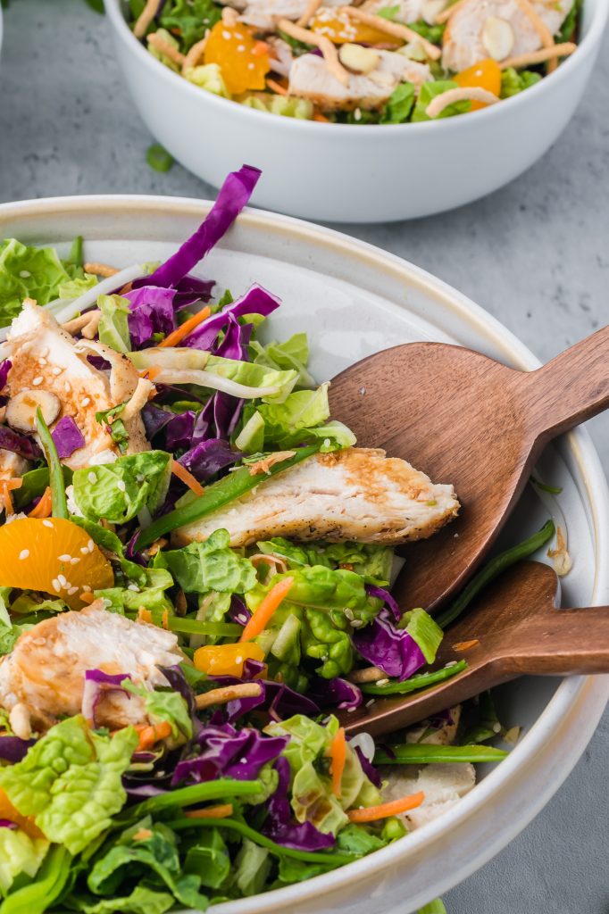 The completed and dressed Chinese Style Chicken Salad with Cabbage in a bowl with wooden salad serving utensils in the bowl.