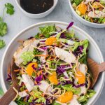 A completed Chinese Style Chicken Salad with Cabbage in a white bowl with the dressing in a small bowl to the side.