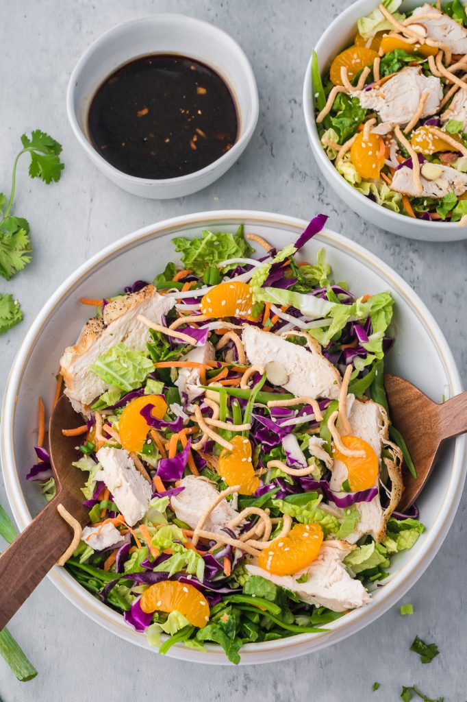 A completed Chinese Style Chicken Salad with Cabbage in a white bowl with the dressing in a small bowl to the side.