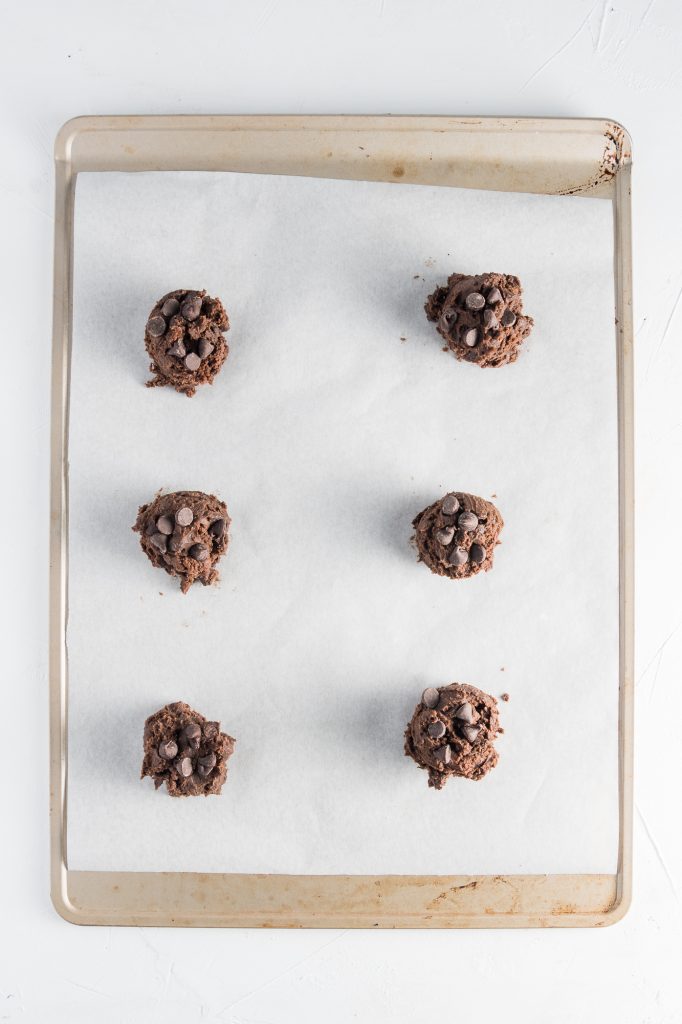 Six scoops of dough on a parchment-lined tray.