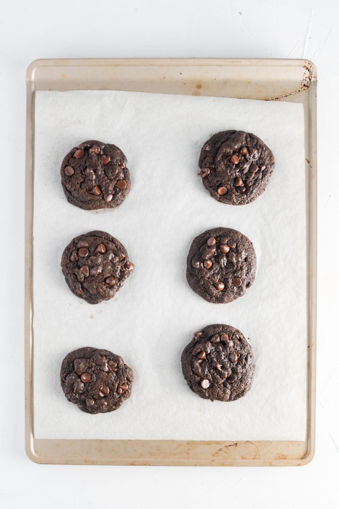 Six baked Chewy Double Chocolate Chip Cookies on a parchment-lined tray.