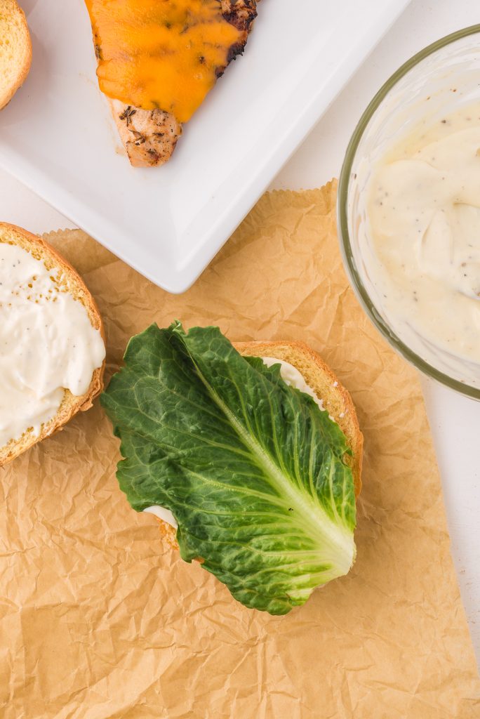 A split hamburger bun topped with garlic aioli, then a piece of lettuce.