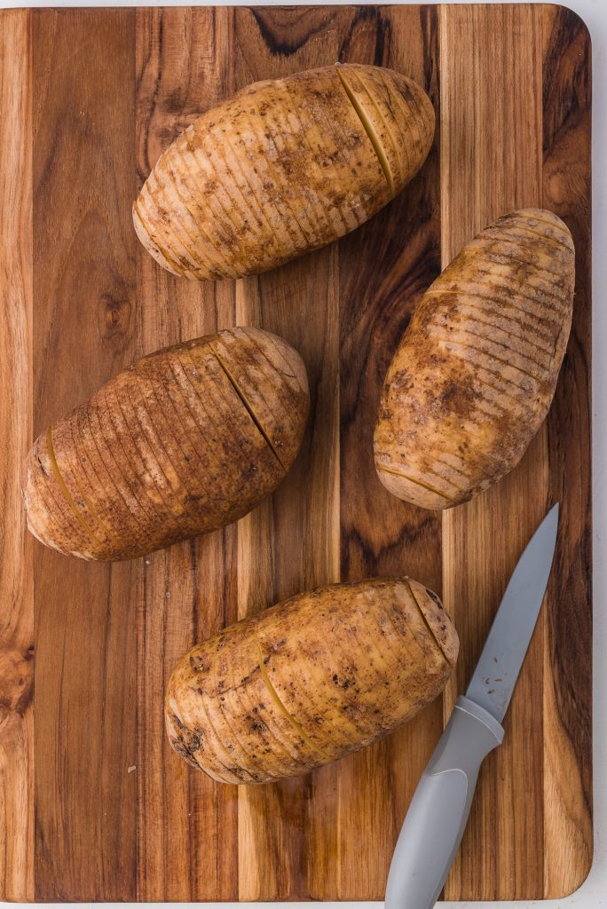 Four potatoes on a cutting board sliced about ⅛" lines with a paring knife.