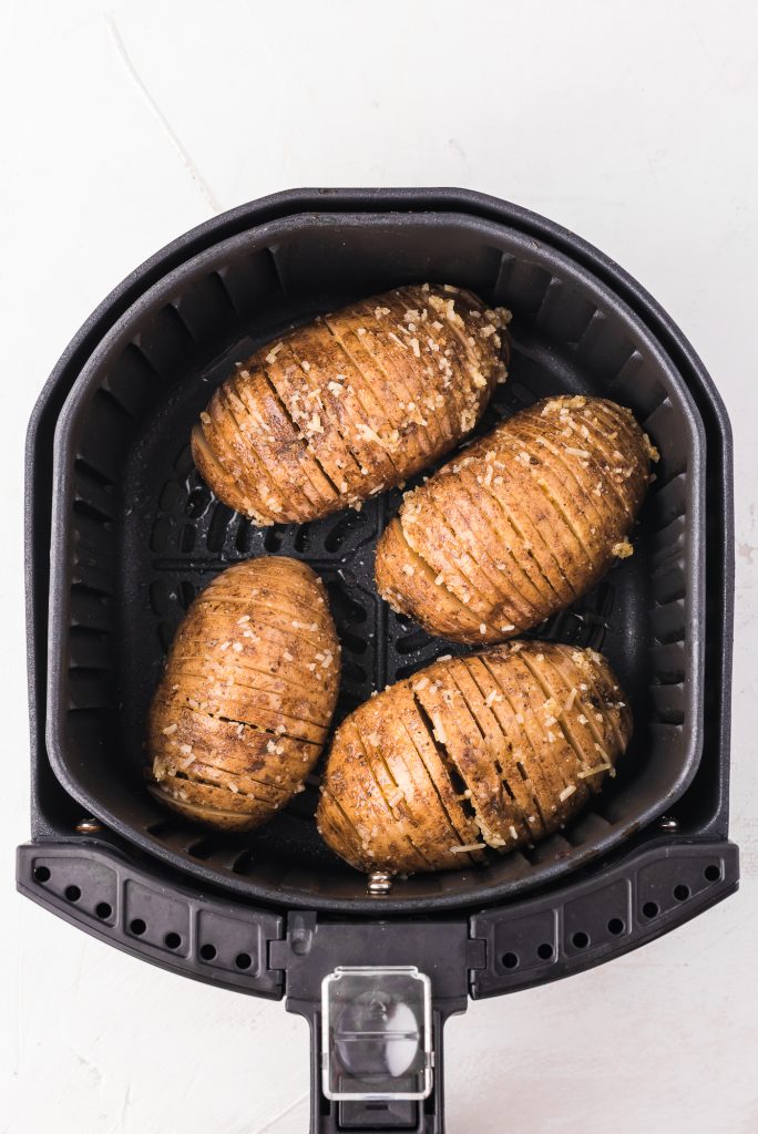 Four sliced and topped potatoes in an air fryer basket.