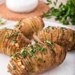 Four Hasselback potatoes on a white plate with parsley topping