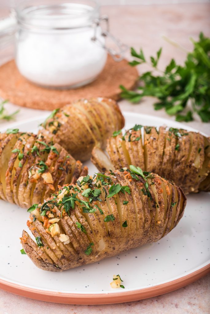 Four Hasselback potatoes on a white plate with parsley topping