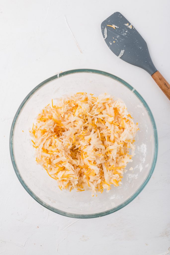 A glass bowl of grated potato, grated onion, and cheese mixture.