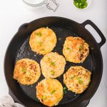 Six Cheesy Potato and Onion Breakfast Pancakes frying in a cast iron skillet.