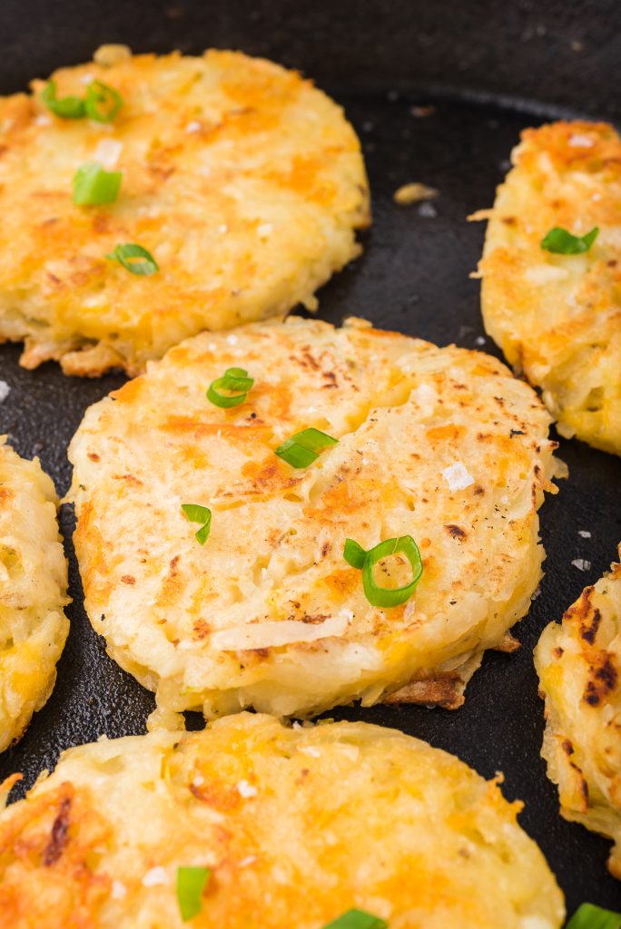 A close-up of Cheesy Potato and Onion Breakfast Pancakes frying in a cast iron skillet.