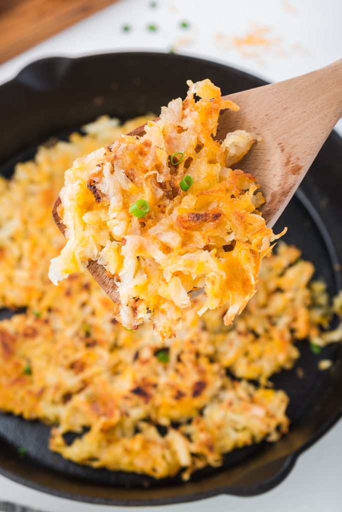 A close up of a wooden spoon holding a spoonful of the Quick Cheesy Homemade Hash Browns.