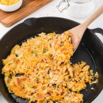 A wooden spoon about to serve the Quick Cheesy Homemade Hash Browns from a cast iron skillet.