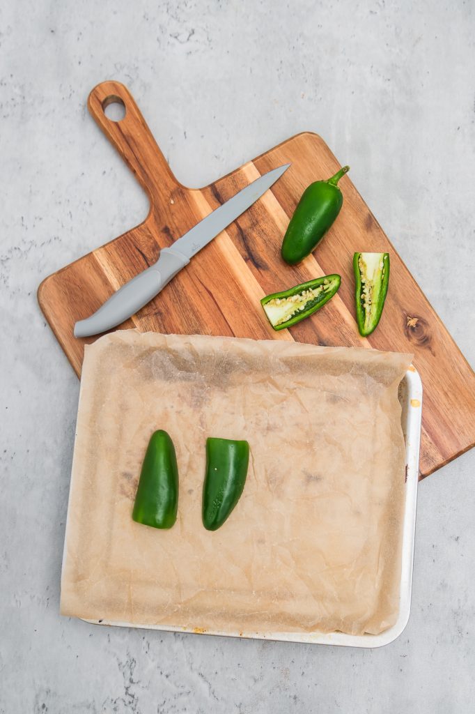 Jalapeño peppers being cut in half lengthwise on a wooden cutting board.