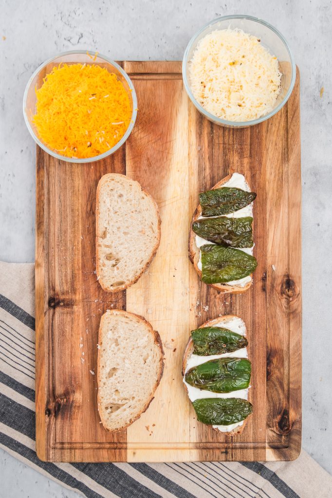 Roasted Jalapeño peppers on the buttered sliced bread on a wooden cutting board.