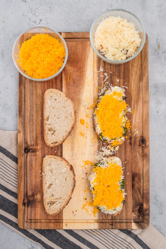 Roasted Jalapeño peppers topped with shredded cheese on the buttered sliced bread on a wooden cutting board.