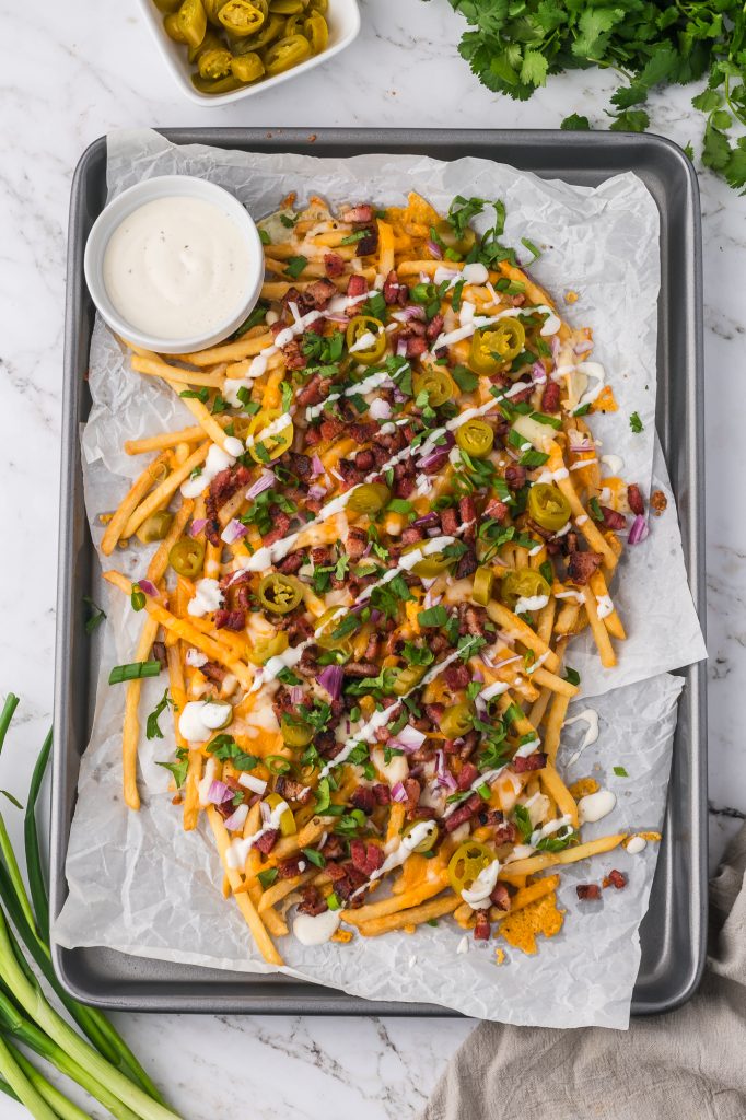 A fully dressed tray of Loaded Cheese Fries with a side of ranch dressing in a cup.