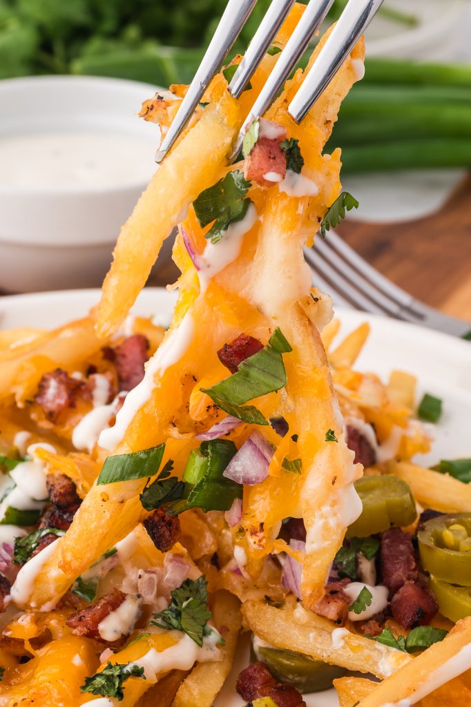 A close up of a fork picking up a bite of Loaded Cheese Fries.