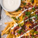 A close up of Loaded Cheese Fries with a side of ranch dressing.