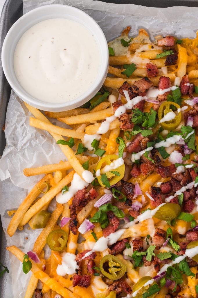 A close up of Loaded Cheese Fries with a side of ranch dressing.