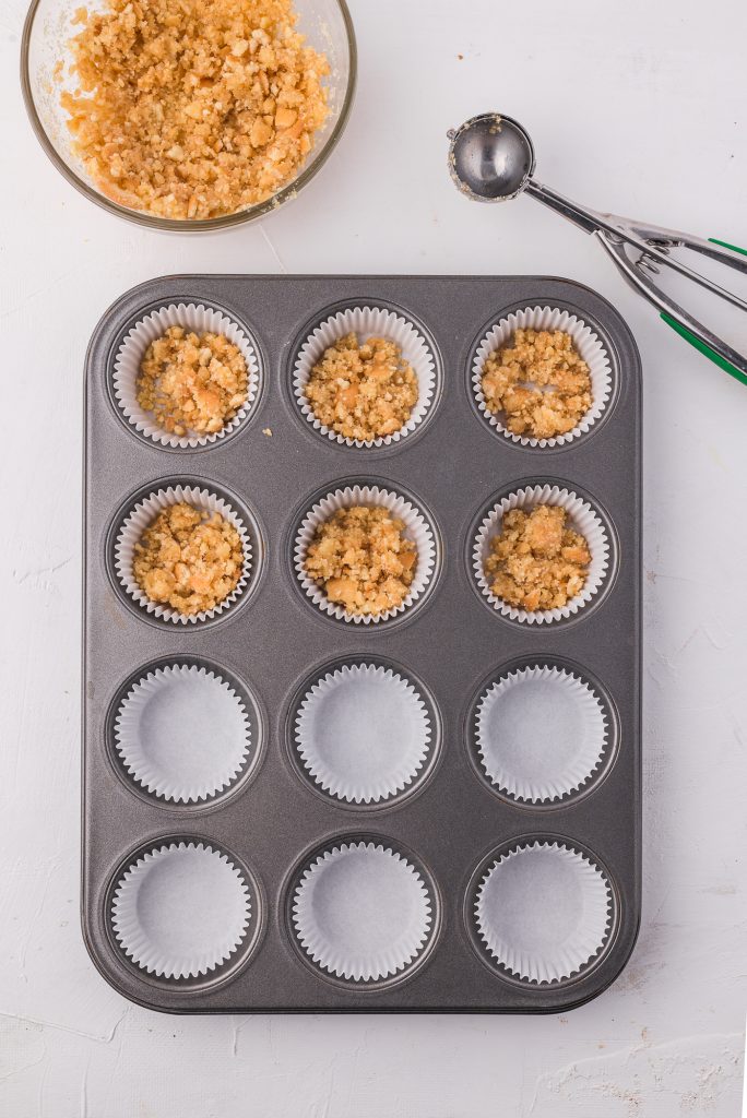 A muffin tin lined with paper cups. Half the cups are filled with crust mixture.