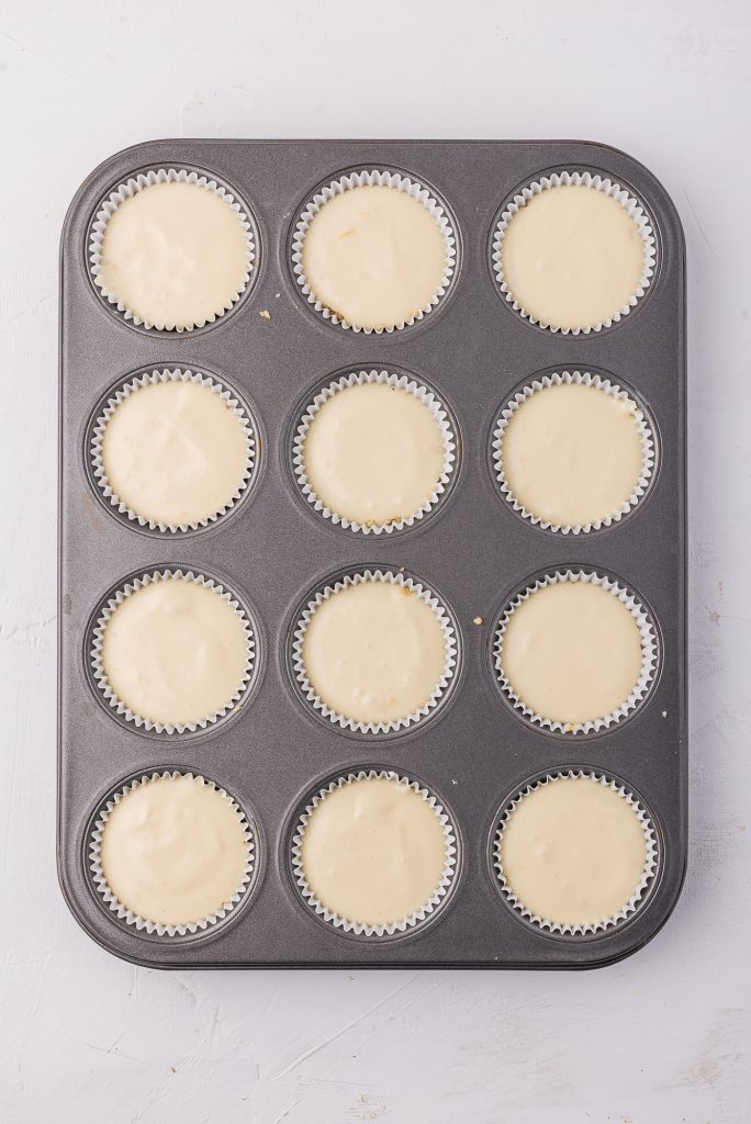 A muffin tin lined with paper cups filled in with the cheesecake mixture.