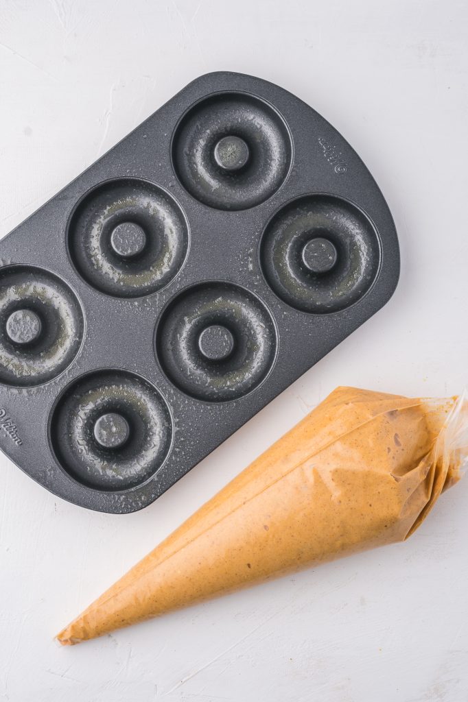 A tube of batter next to an oiled donut pan.